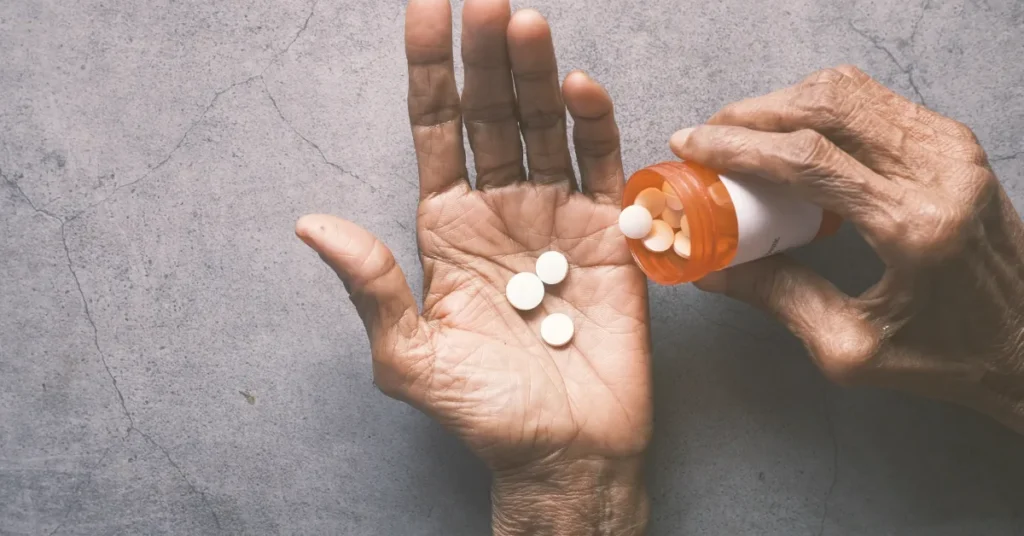 Mão aberta recebendo comprimidos brancos de um frasco laranja, representando o uso de suplementos.